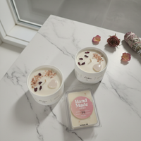 Two small candles with decorative elements on a marble surface, accompanied by a 'Hand Made' sign.