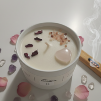 Candle in a white container with decorative stones and petals on a light surface